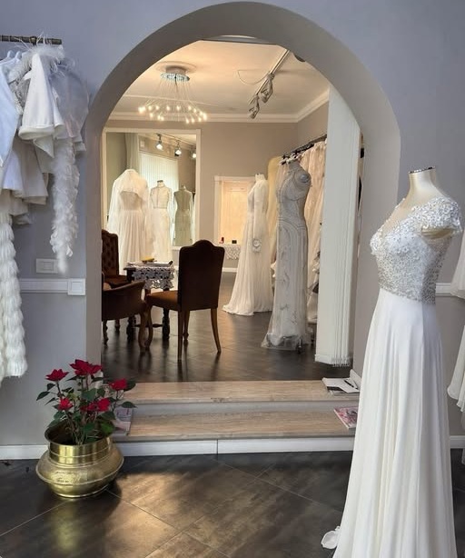Interno dell'Atelier Piras 1953 con arco, manichino in abito bianco ricamato, rose rosse e salottino sotto lampadario